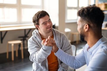 Two individuals smiling and clasping hands in a supportive gesture